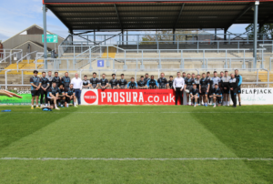 The Wakefield Trinity Rugby League Football Club's first team pictured around the Prosura advertising banner alongside Jon Newall, CEO of Prosura, and Callum Topliss, Commercial Account Executive at Prosura.