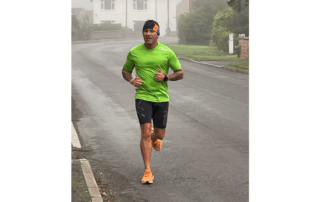 An image of Paul running along the street in a black bandana, lime green top, shorts and orange trainers.